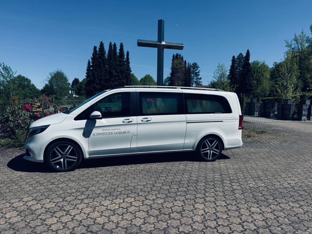 Weißer Mercedes V-Klasse Bestattungswagen des Bestattungshauses Schweitzer vor dem Friedhofskreuz in Saarlouis